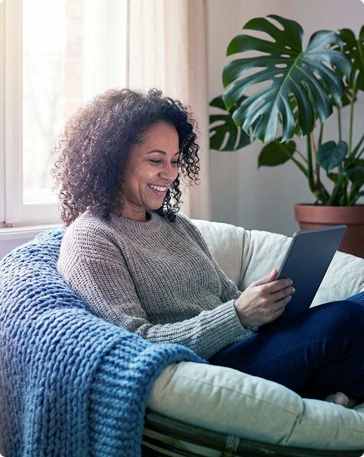 Woman smiling on a sofa with a laptop, reading in a cozy living room with a plant nearby