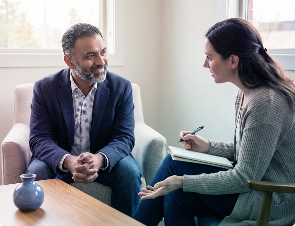 Two people in a 상담 session, seated across from each other with a notebook and pen in a bright room