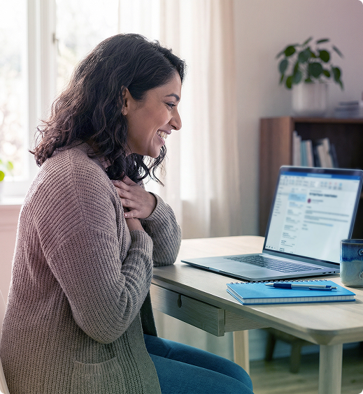 Woman seated at a desk, smiling at a laptop in a bright home office.