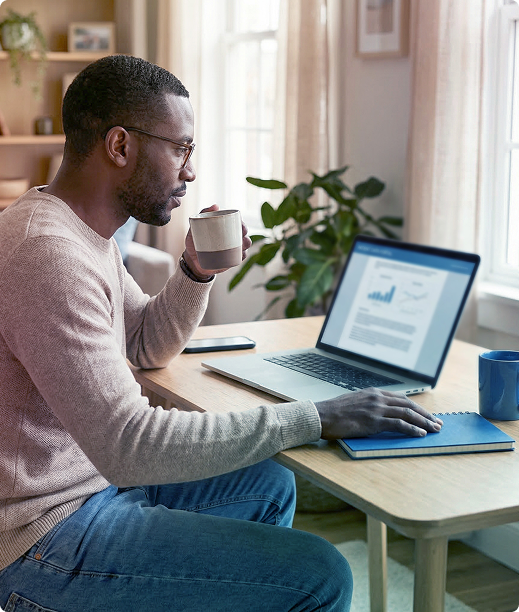 Person working on a laptop at a desk, holding a mug in a bright home office