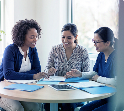 Three coworkers review documents and a laptop at a round table in a bright office