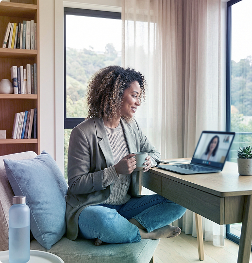Person video chatting from a cozy home office with laptop, mug, and large window view