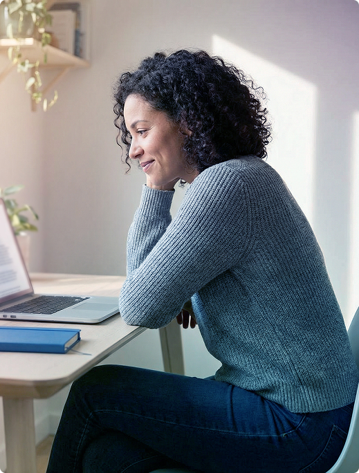 Person sitting at a desk, leaning on a hand and working on a laptop in a bright room.