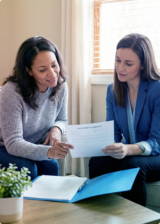 Two people reviewing a document at a desk in a bright office, with an open notebook and potted plant nearby.