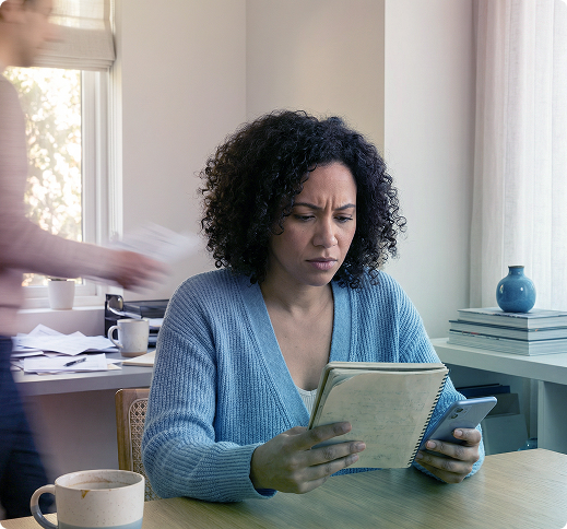 Two people smiling in a bright office, talking across a small table with mugs and a notebook.