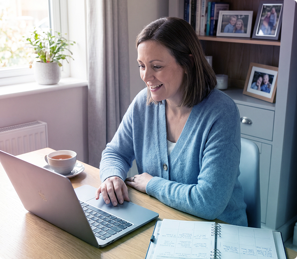 Woman reading a document at a desk beside a window, with a mug and blue notebook nearby.
