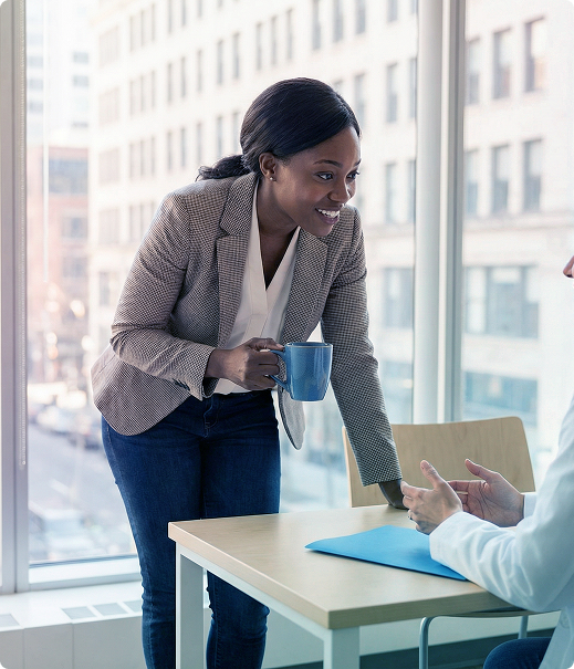 Colleague smiling with a blue mug during a meeting at a table by large office windows