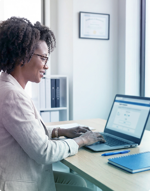 Person typing on a laptop at a bright office desk with a notebook nearby.