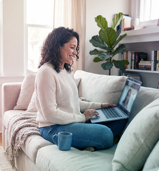 Woman sitting on a couch using a laptop in a bright living room, with a mug nearby.