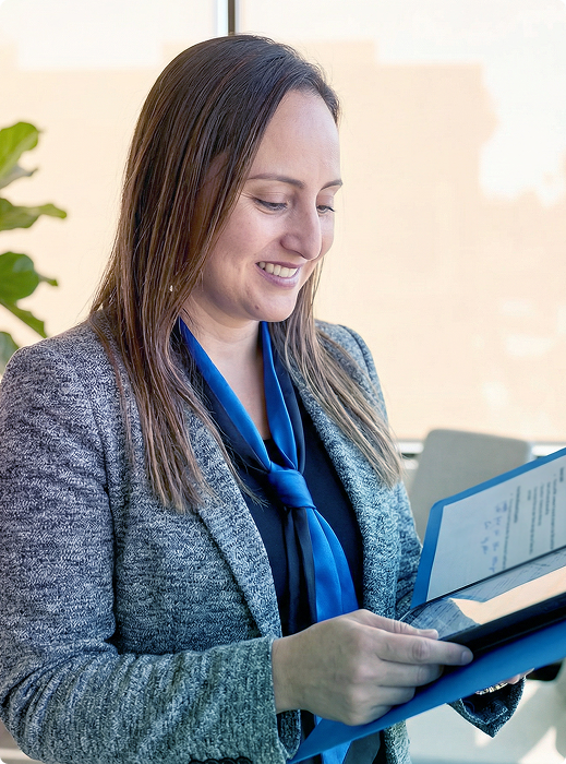 Woman in a gray blazer smiling while reading a blue folder indoors
