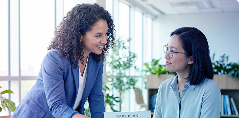 Two coworkers talking and smiling in a bright office near a window