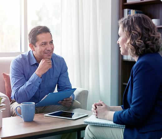 Two people talking at a table with coffee and a tablet in a bright office setting