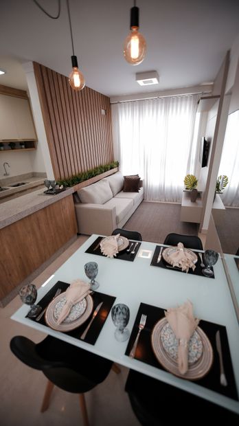 Modern dining area with a glass table set for four, pendant lights, and a sofa by a bright window.