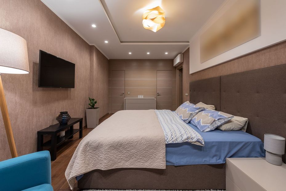 Modern bedroom with a bed, wall-mounted TV, wood flooring, and warm recessed lighting