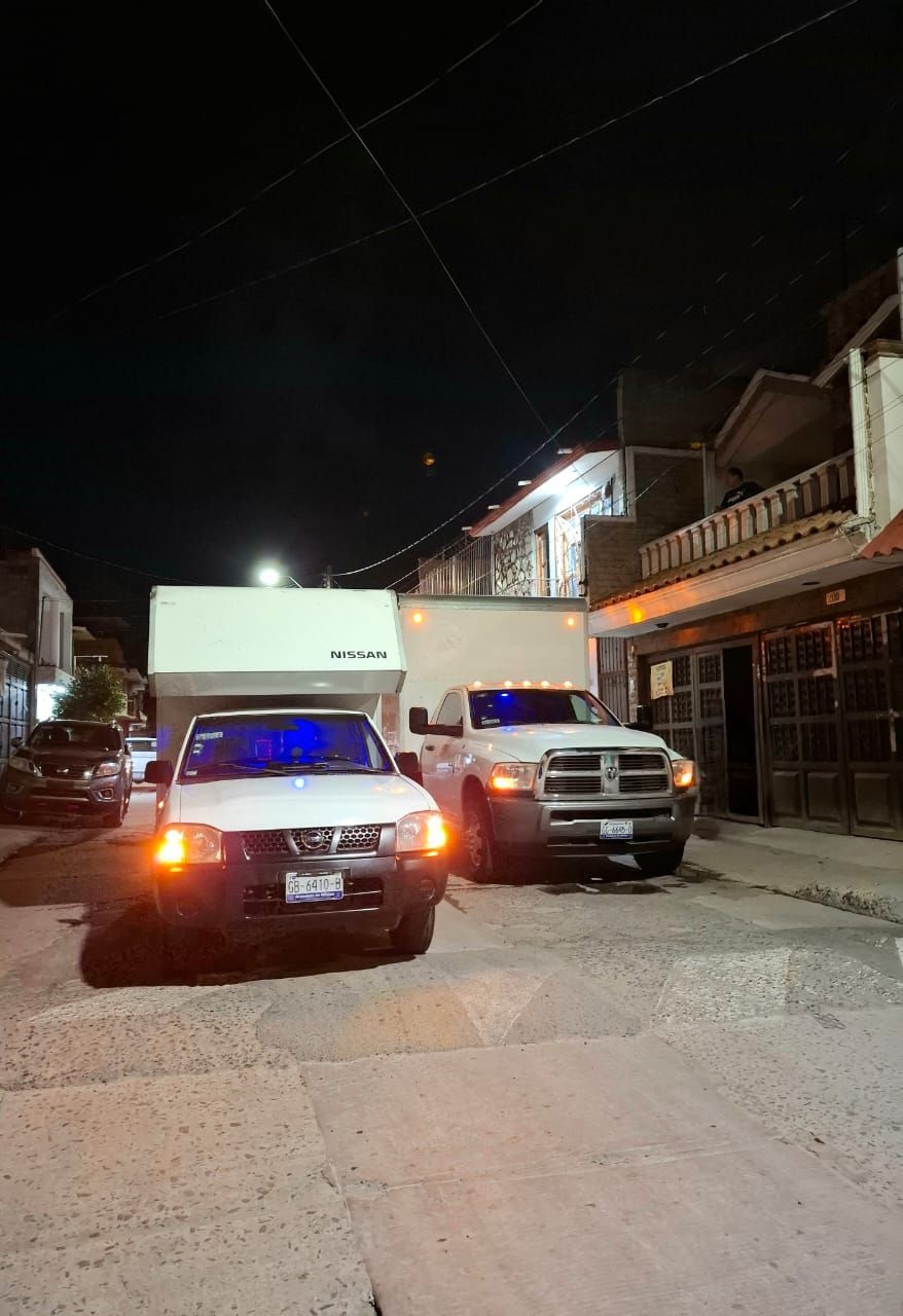 Dos camiones blancos están estacionados al costado de la carretera por la noche.