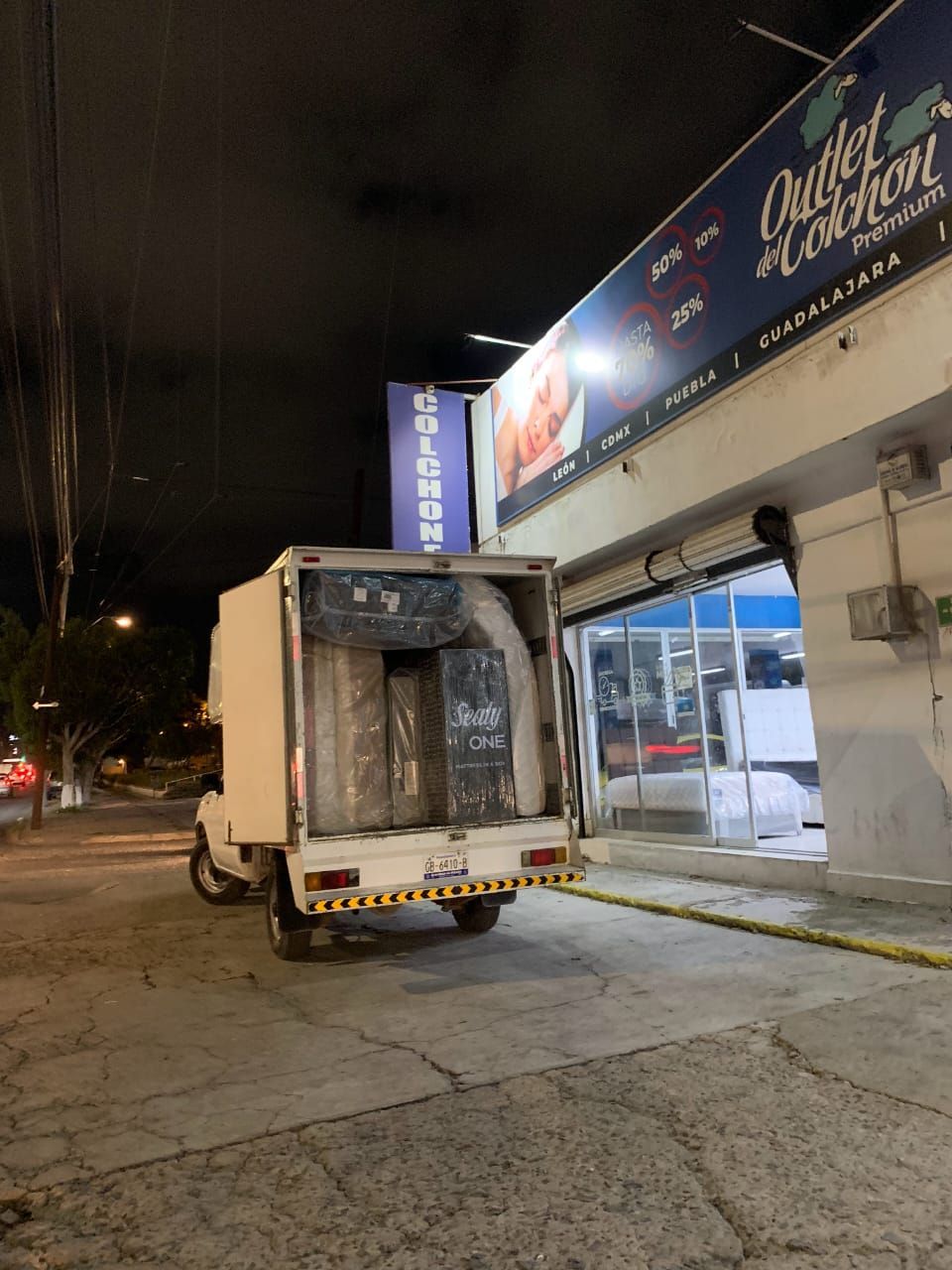 Un camión blanco está estacionado frente a una tienda por la noche.