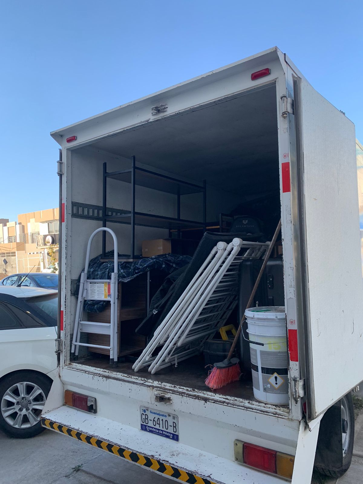 Un camión blanco con una escalera y un balde en la parte trasera está estacionado en un estacionamiento.