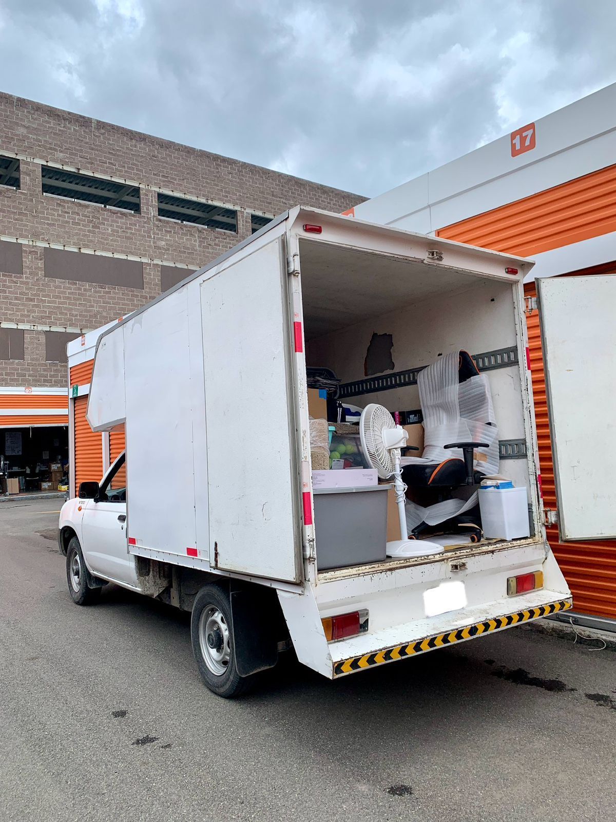 Un camión blanco está estacionado frente a un edificio con la puerta trasera abierta.