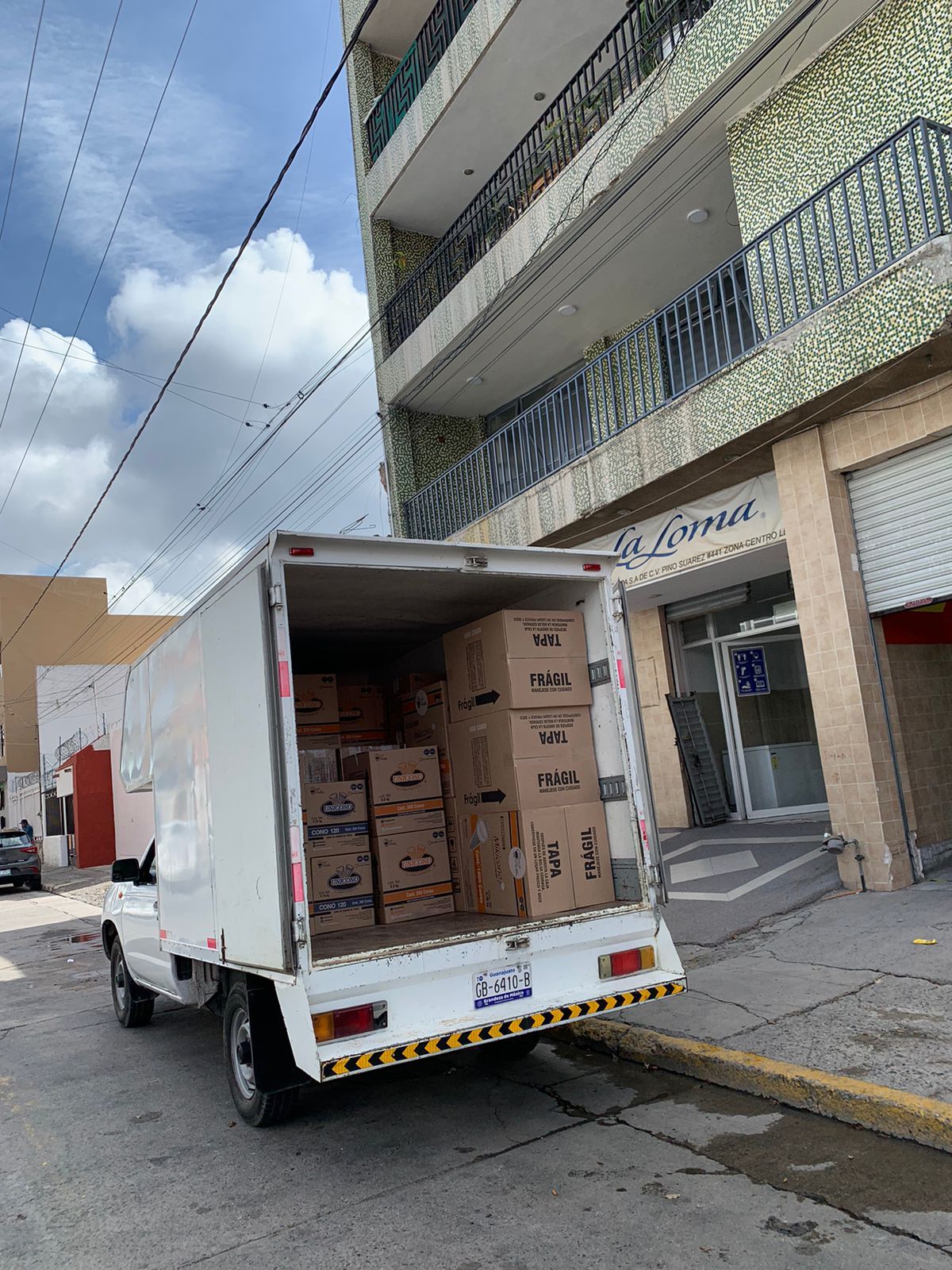 Un camión blanco lleno de cajas está estacionado al costado de la carretera frente a un edificio.