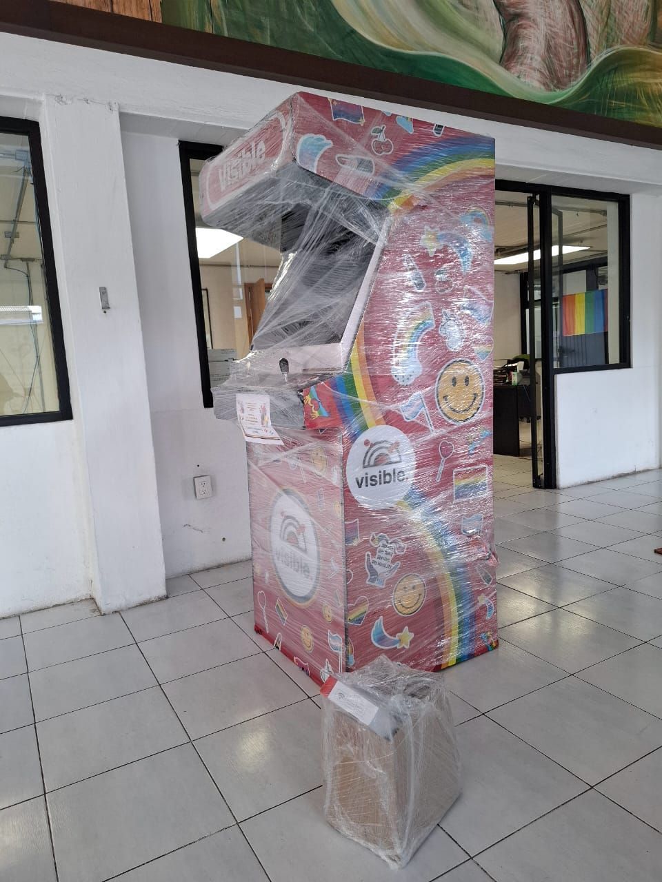 Una máquina arcade de color rosa se encuentra sobre un piso de baldosas en una habitación.