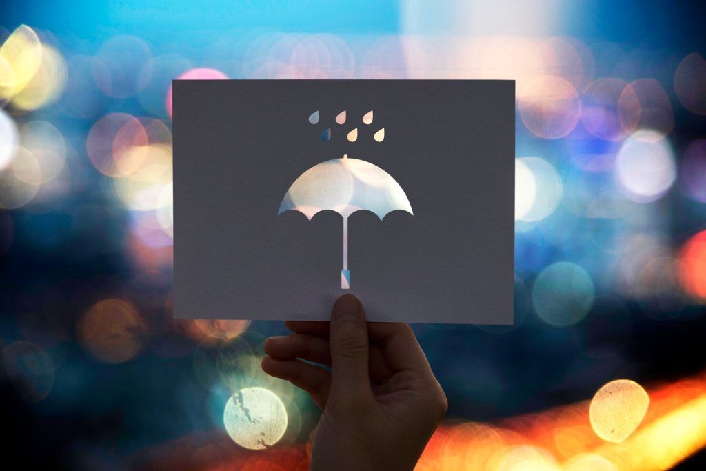 Hand holding a card cut with an umbrella and raindrops, set against blurred city lights.