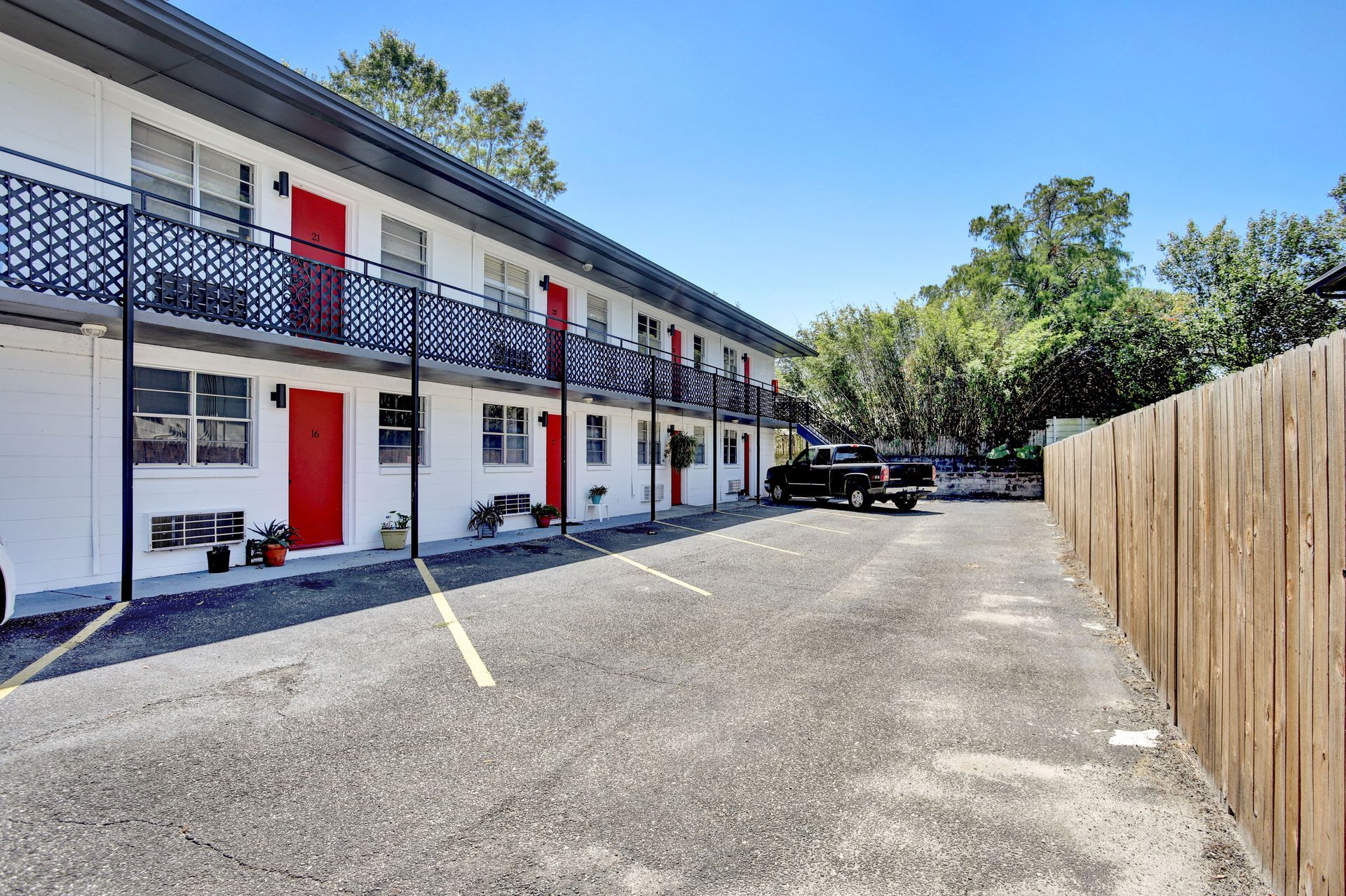 Exterior of a two-story white building with red doors and black metal balconies, asphalt parking lot.