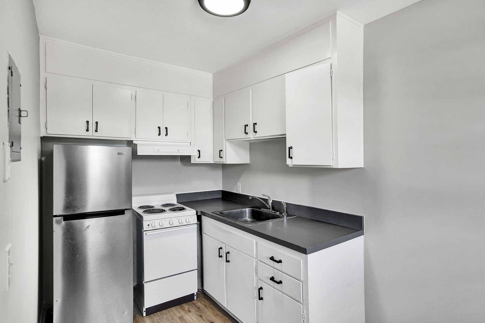 Small, white kitchen with stainless steel refrigerator and gas range. Black countertop and cabinets.