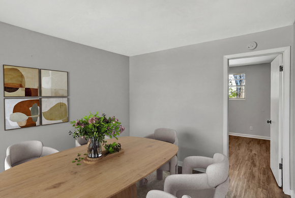 Dining room with wooden table, gray chairs, artwork, and doorway to another room.