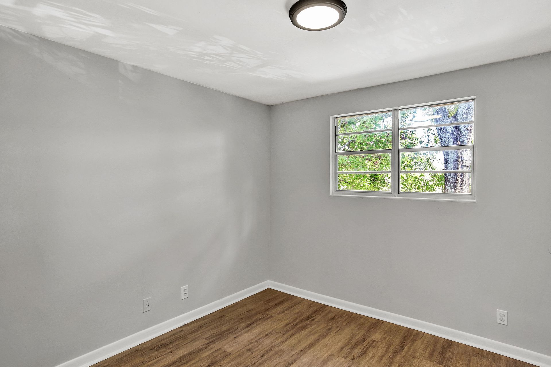 Empty room with gray walls, wood-look floor, window, and a ceiling light.
