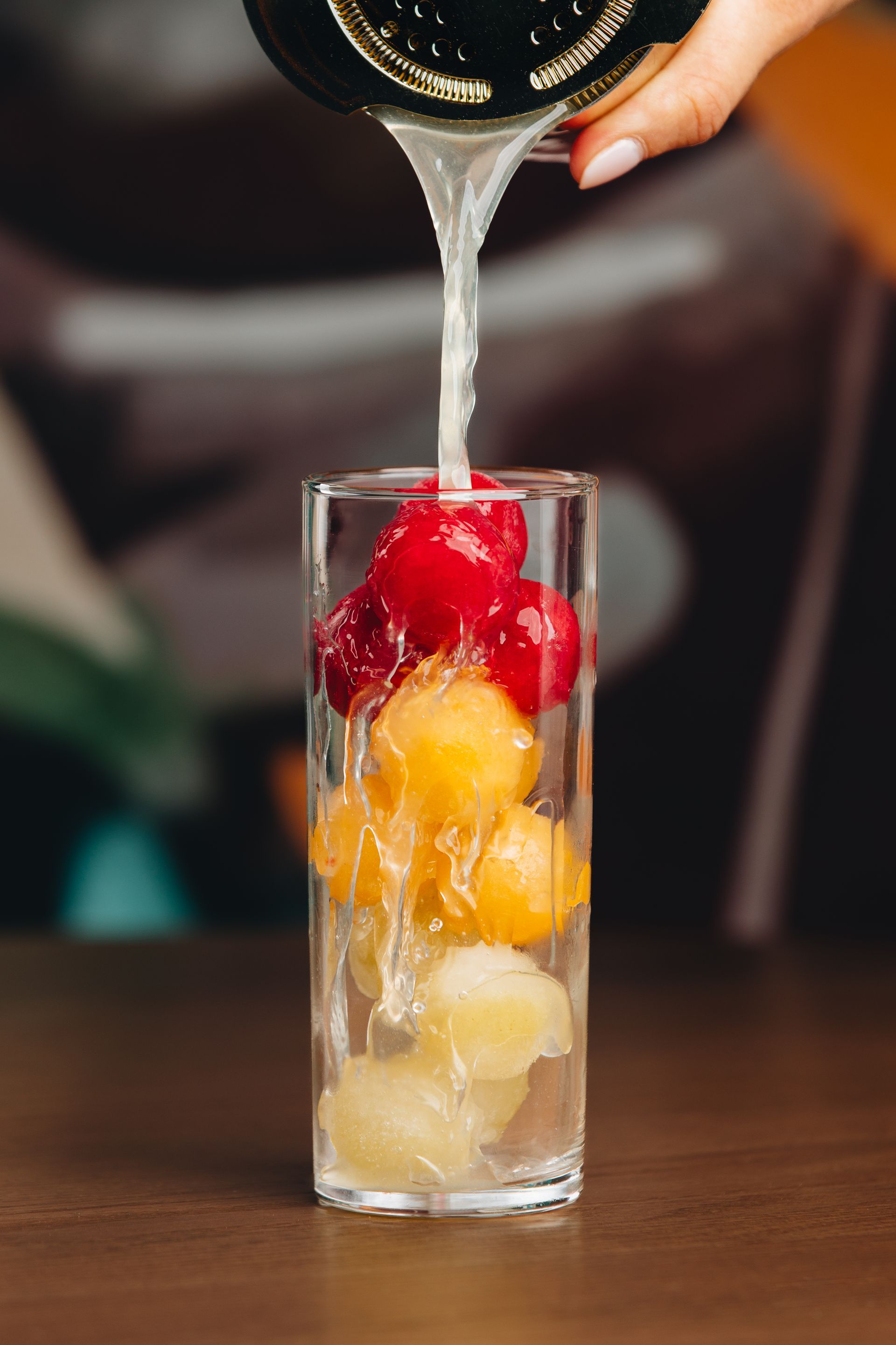 a person is pouring liquid into a glass filled with fruit .