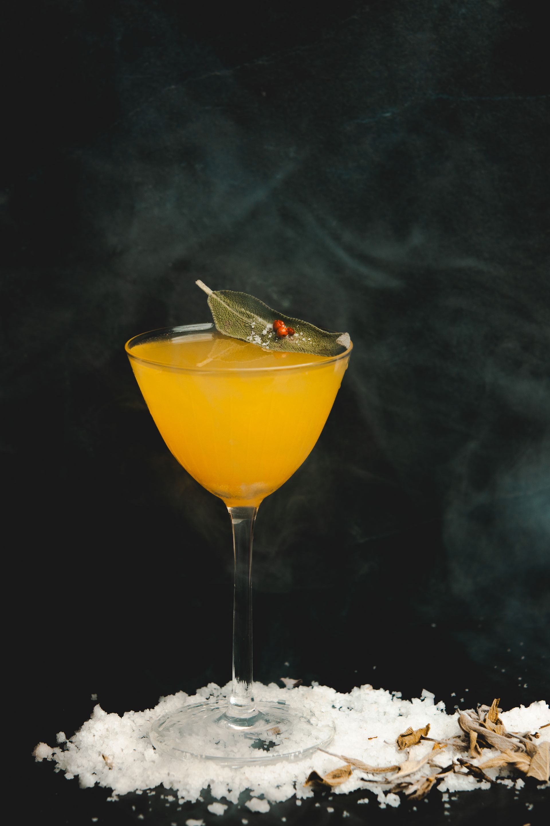 Yellow color alcoholic drink served in a glass with a green garnish