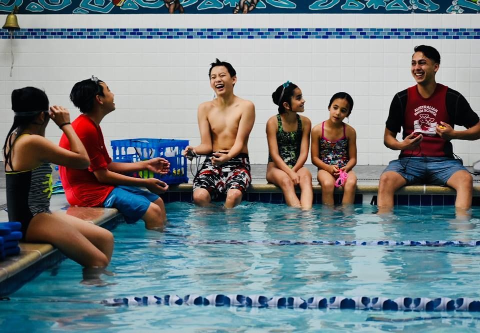 A group of people are sitting on the edge of a swimming pool.