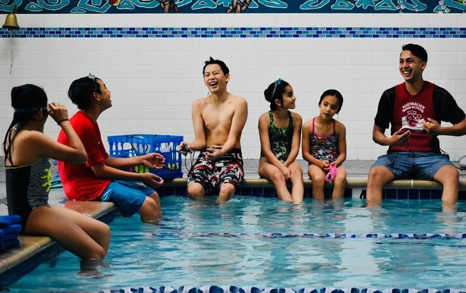 A group of people are sitting on the edge of a swimming pool.