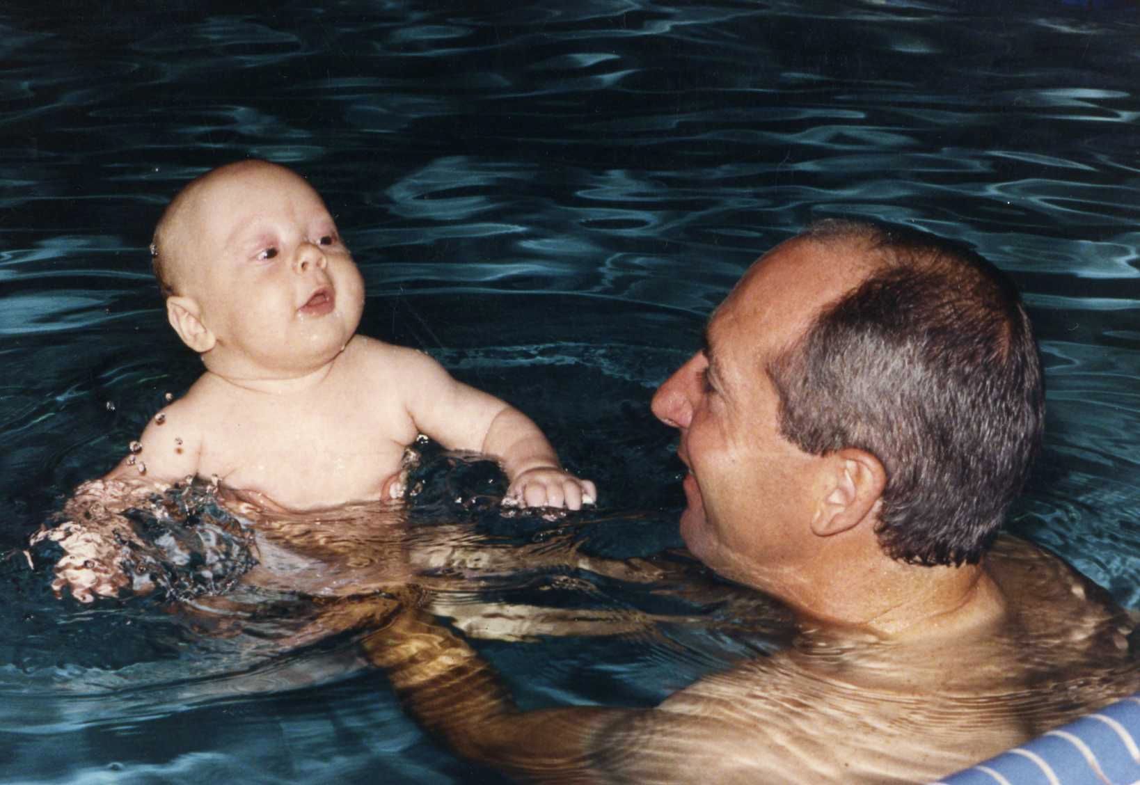 A man is holding a baby in a swimming pool.