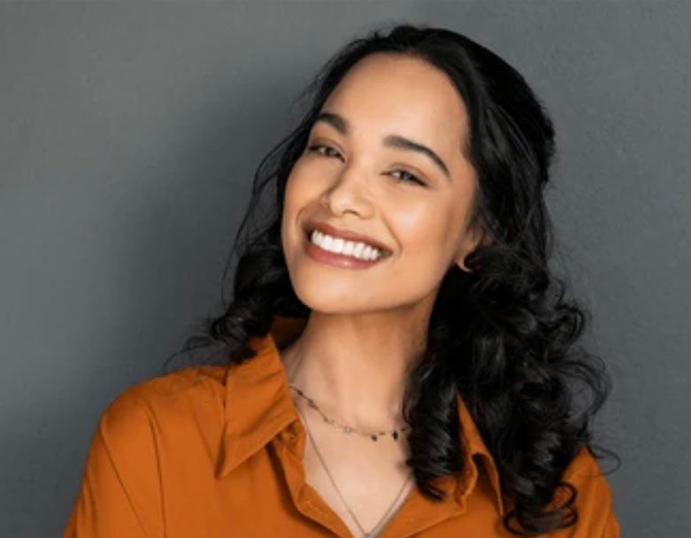 A woman in an orange shirt is smiling for the camera.