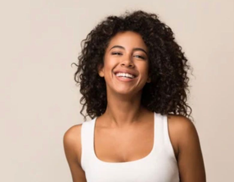 A woman with curly hair is smiling and wearing a white tank top.