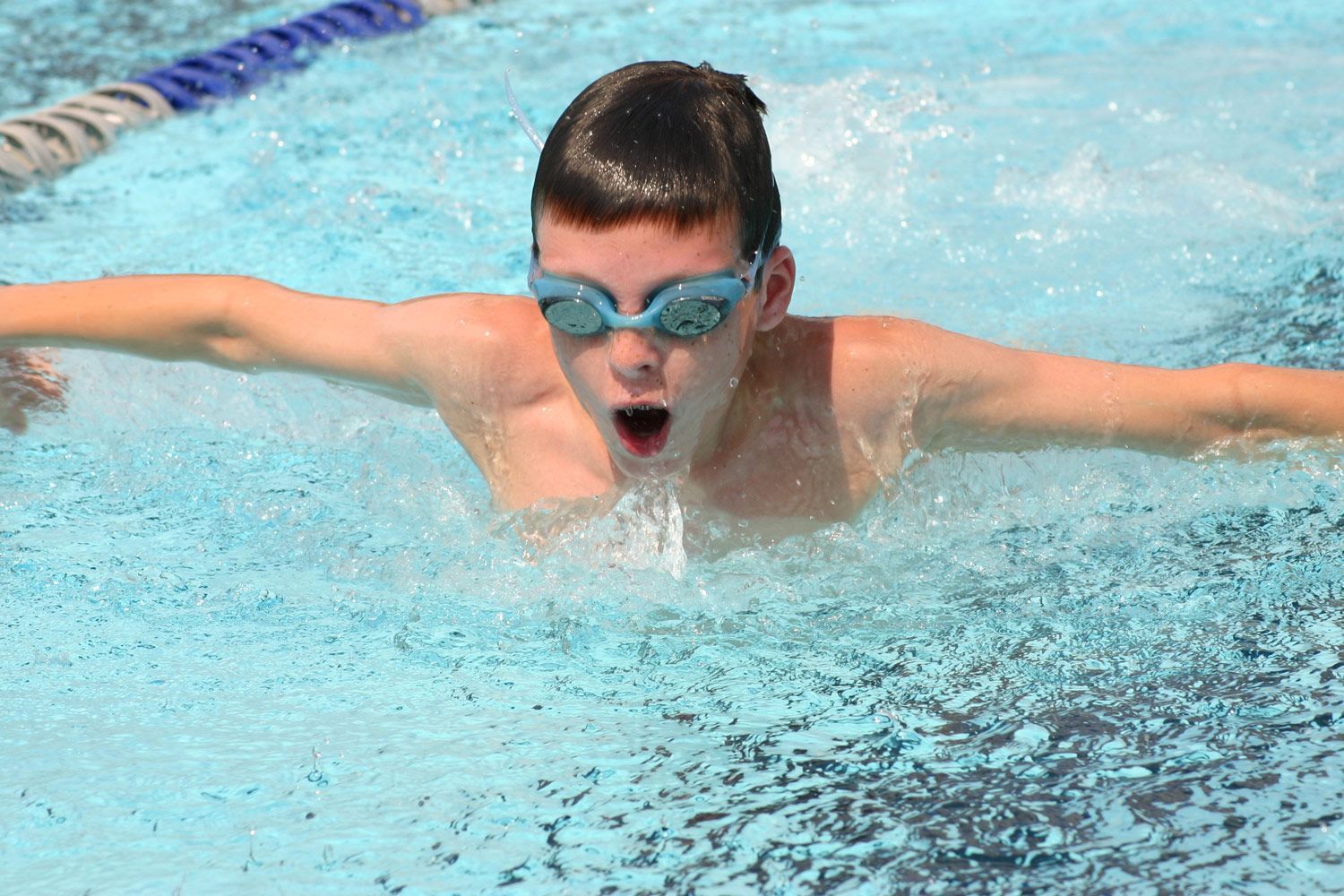 A young boy is swimming in a swimming pool wearing goggles.