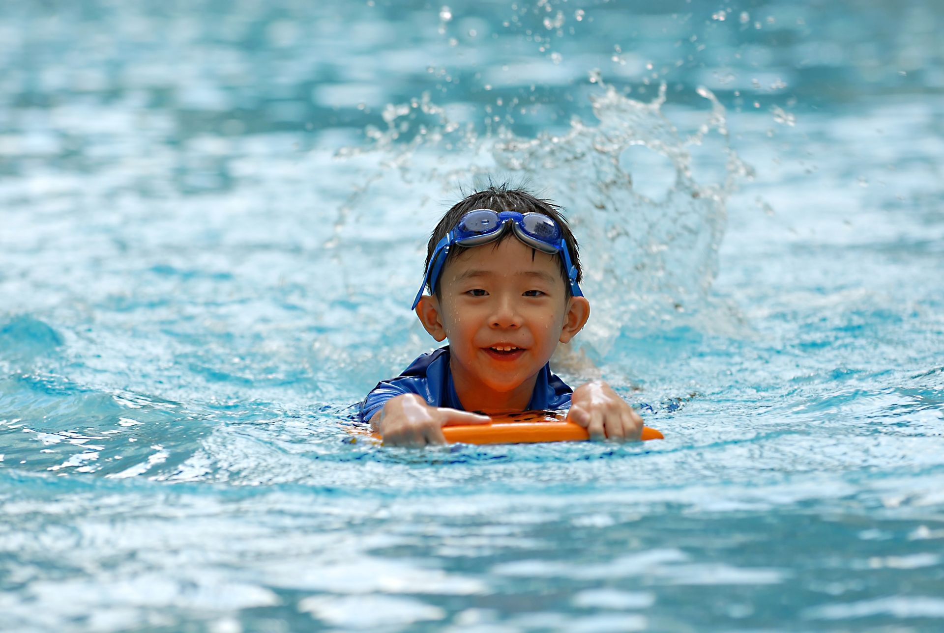 A young boy is swimming in a pool with a boogie board.