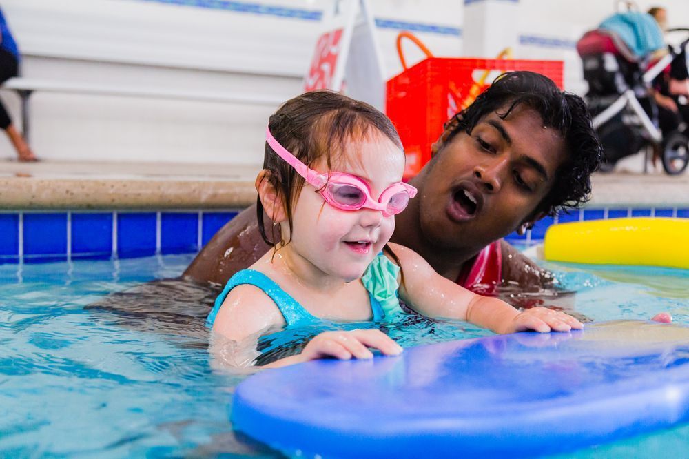 A man is teaching a little girl how to swim in a swimming pool.