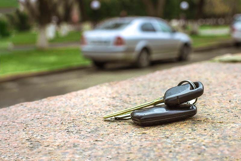 A pair of car keys are laying on the ground next to a car.