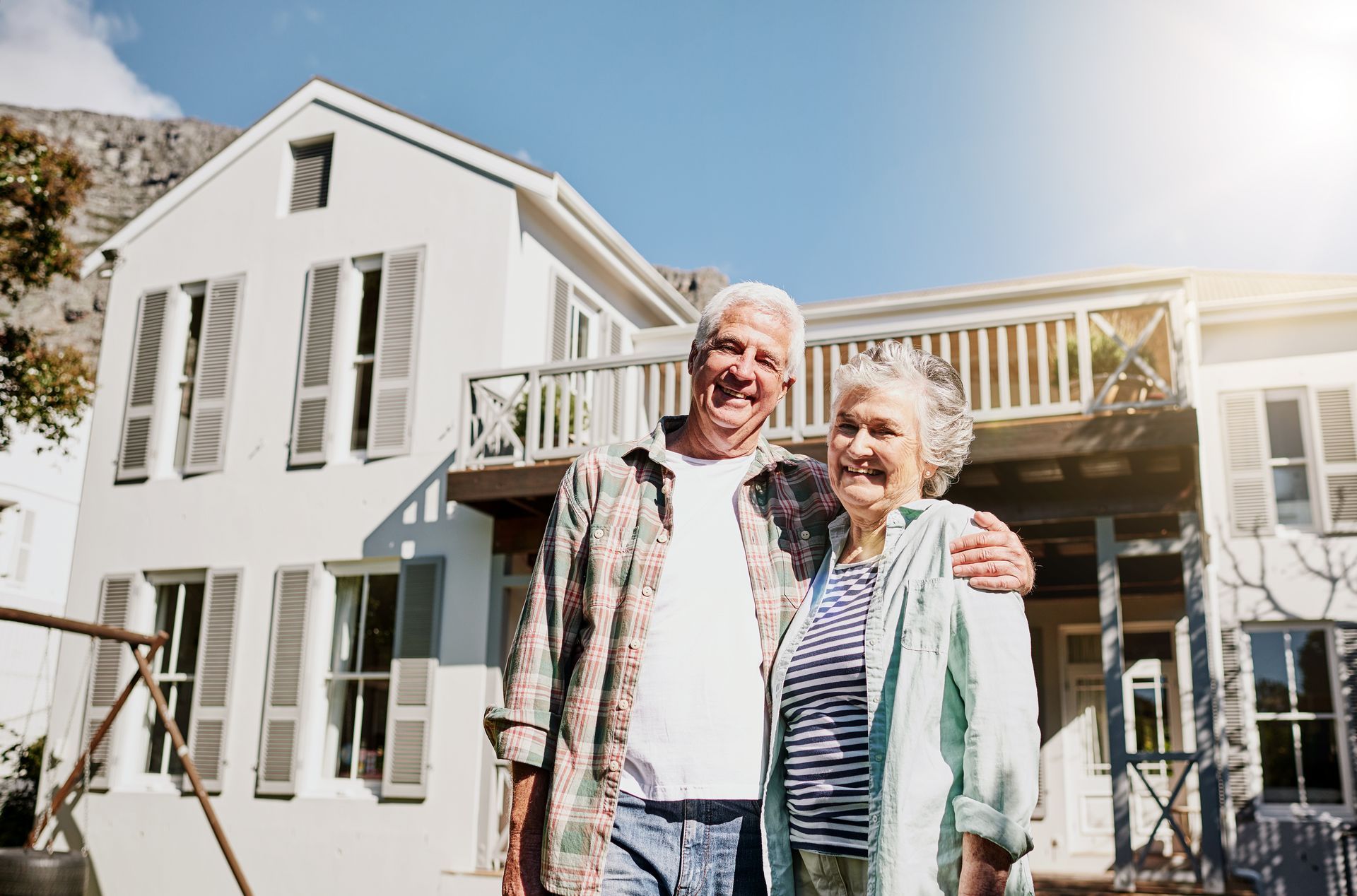 An elderly couple is standing in front of a house.