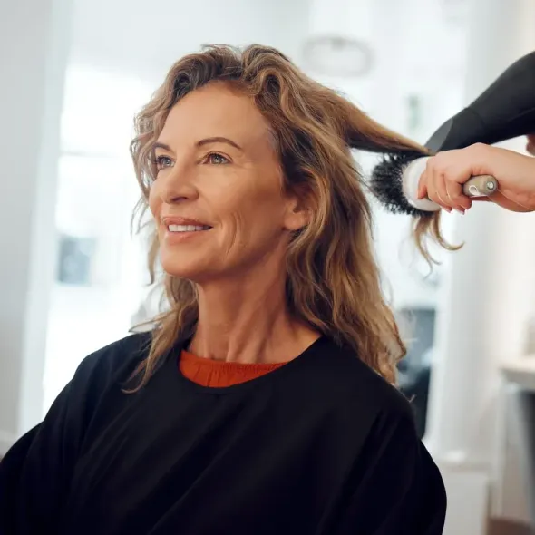 Woman smiling while getting her hair brushed in a bright salon