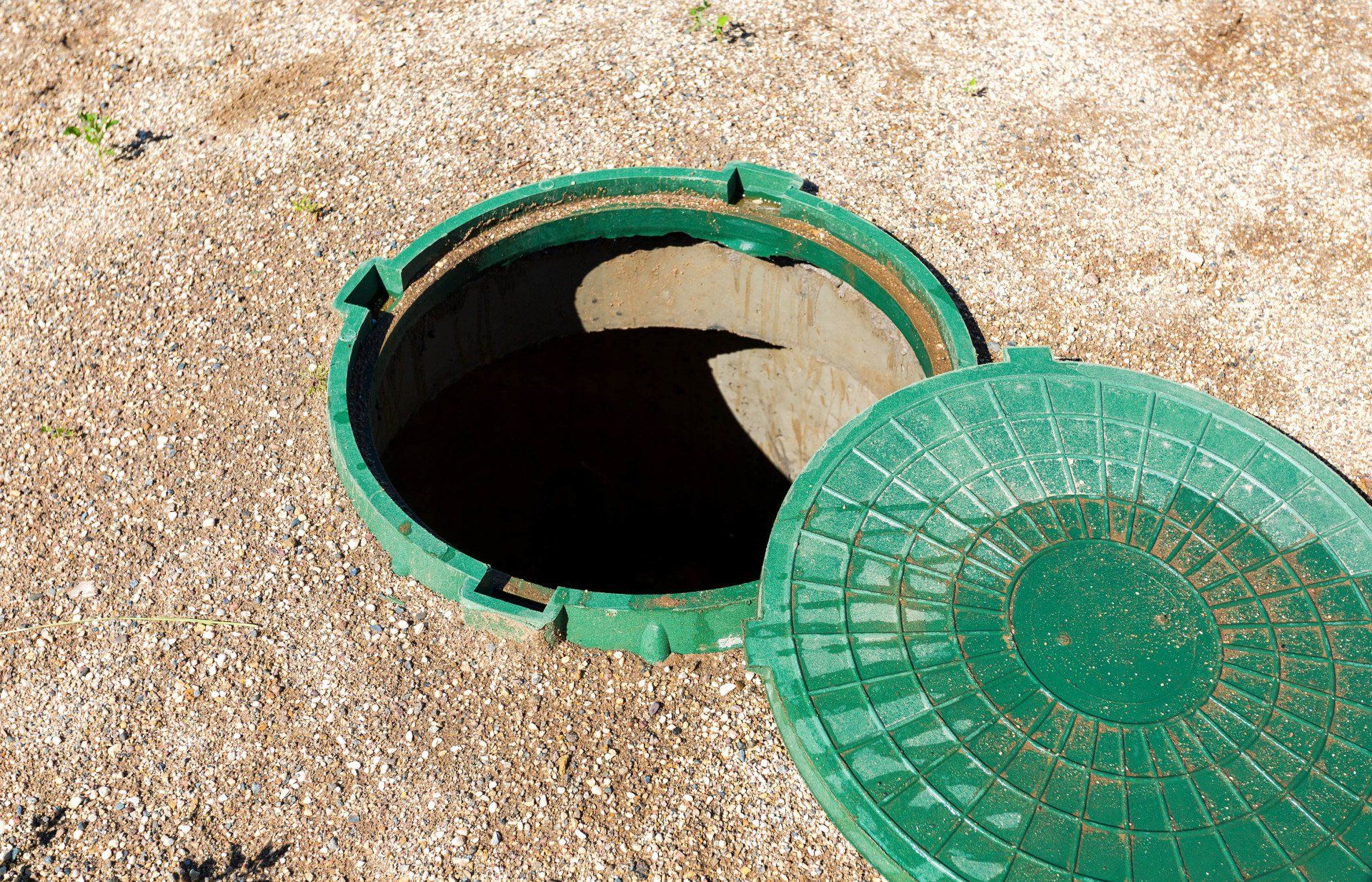 A green manhole cover is open to a hole in the ground.