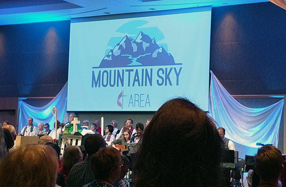 A group of people are sitting in front of a large screen that says mountain sky