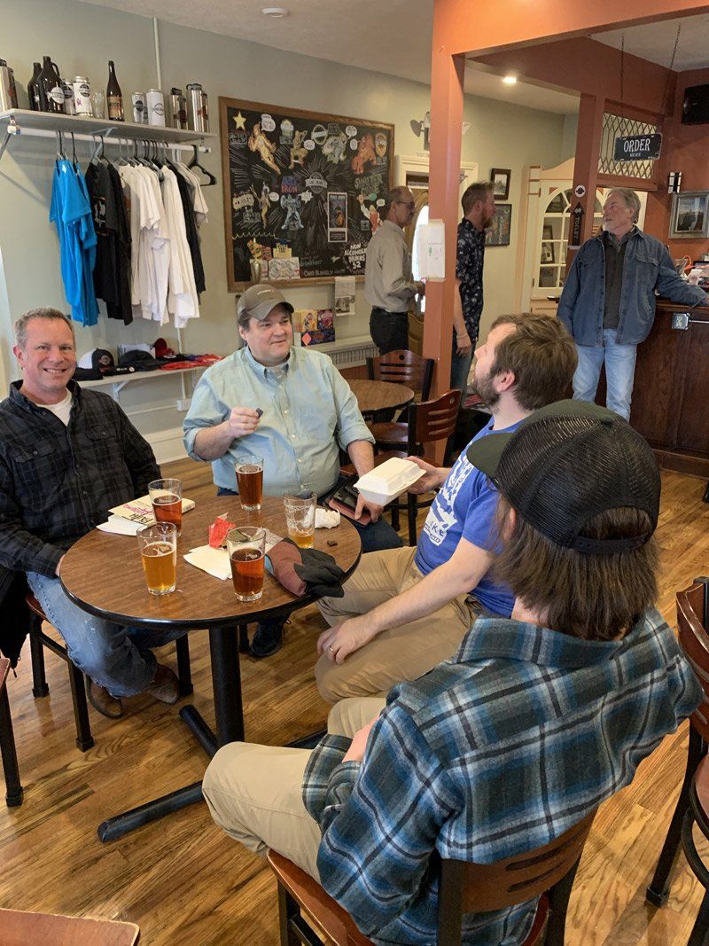 A group of men are sitting at tables in a restaurant drinking beer.