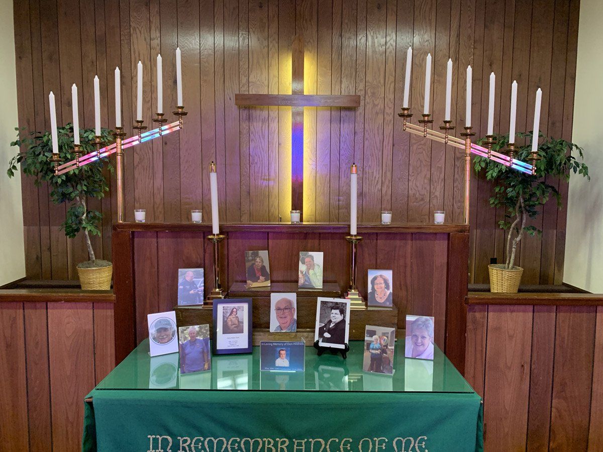 A table with pictures and candles on it in front of a wooden cross at the alter
