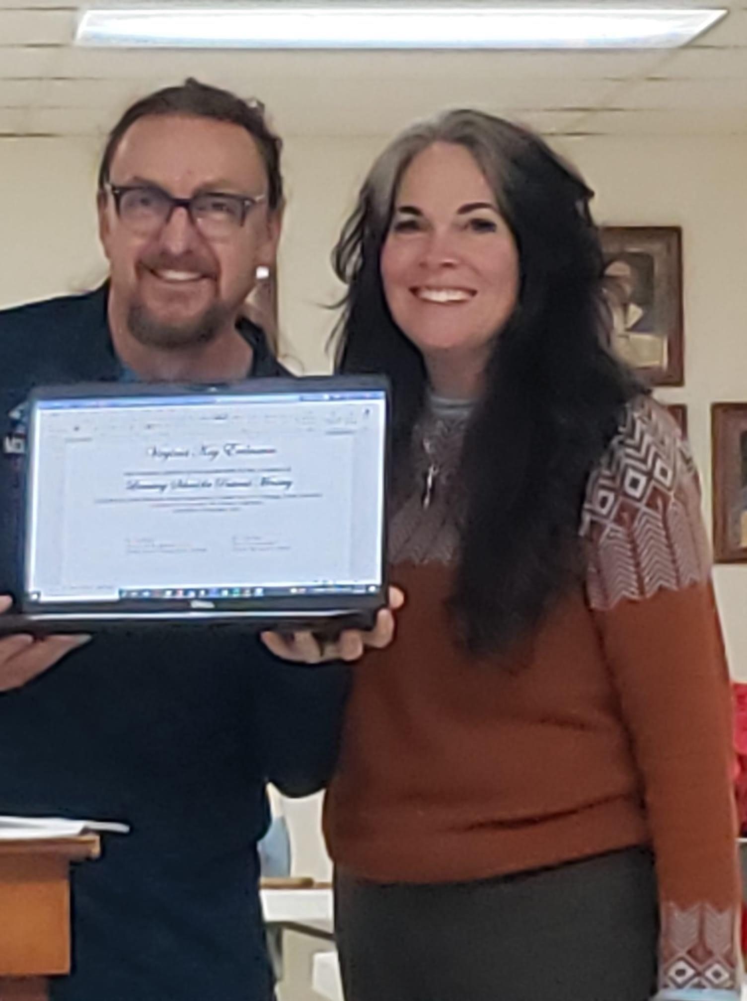 A man and a woman are standing next to each other holding a laptop.