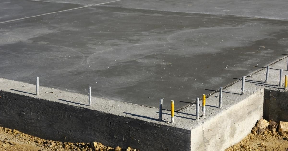Concrete foundation with metal rods set in the edge, ready for construction.