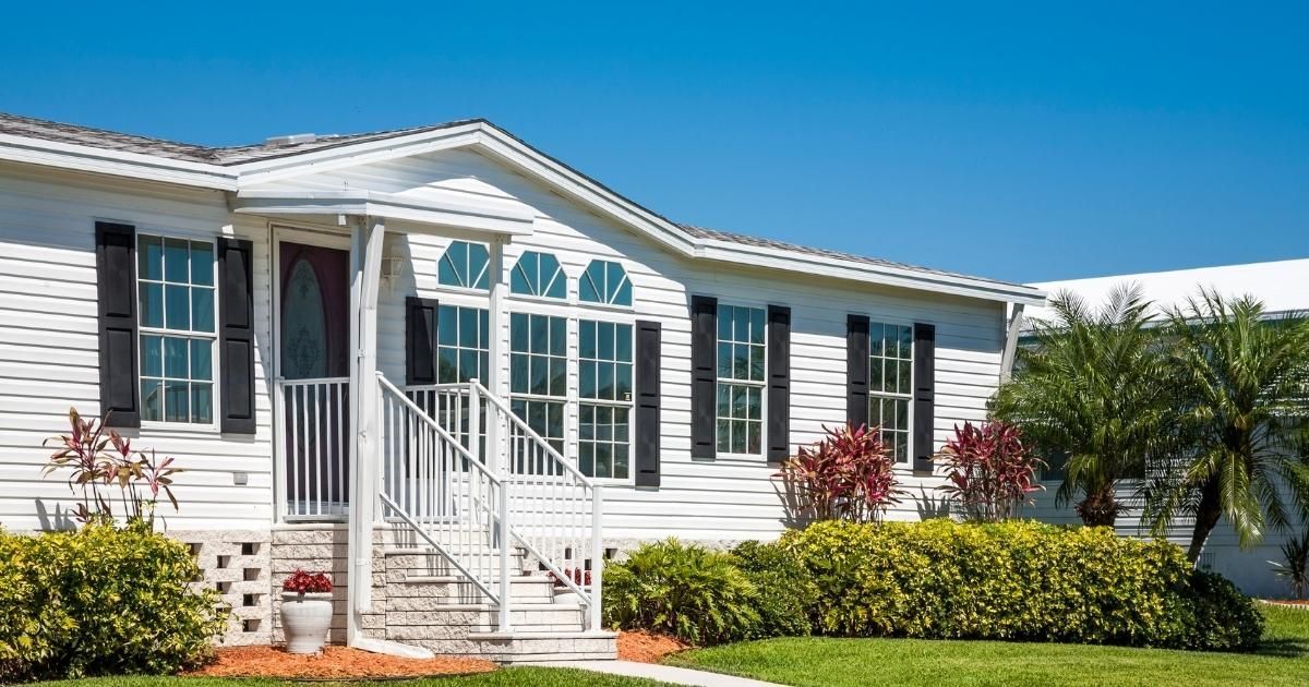 White mobile home with black shutters, blue sky, and green lawn.