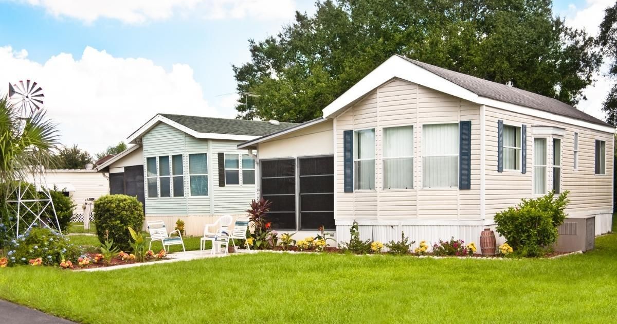 Two beige mobile homes with blue shutters and a small garden in front.